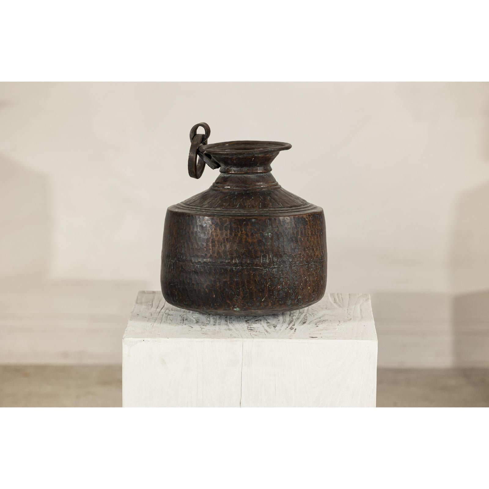 Vintage silver hand-hammered metal jug with ring handle on a white pedestal.