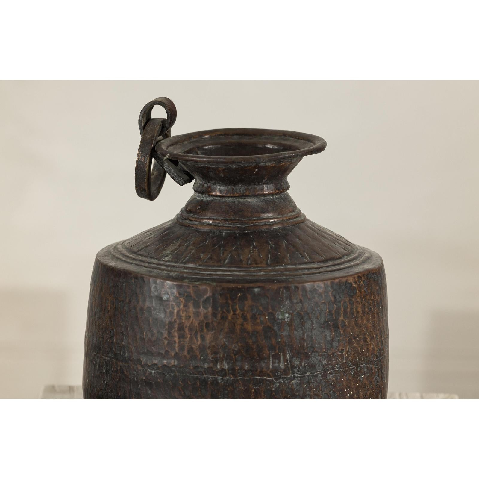 Close-up of a silver hand-hammered metal jug with ring handle, wide spout, and textured finish.