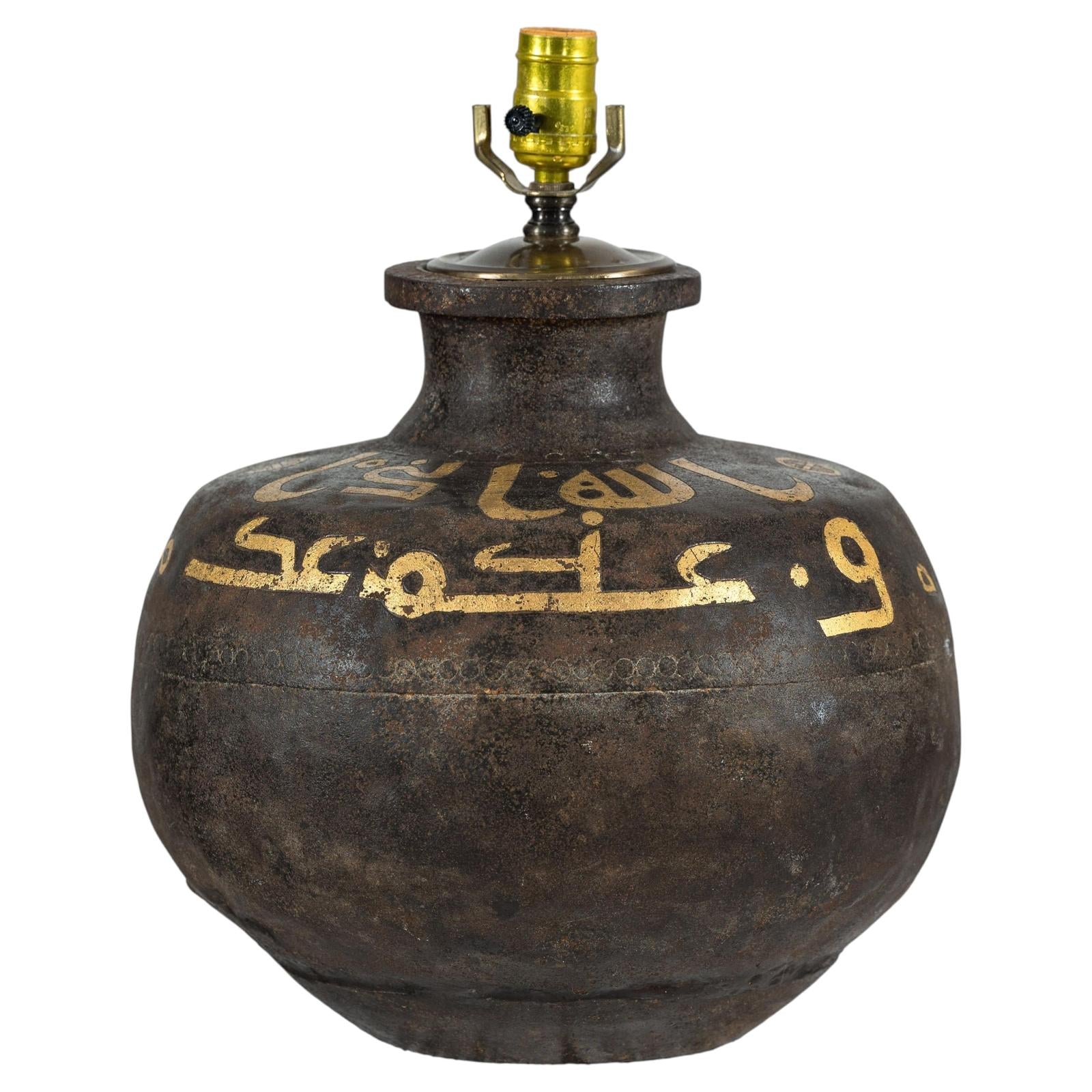 Close-up of a vintage brown metal jug lamp with gold Arabic script and brass socket, patina visible.