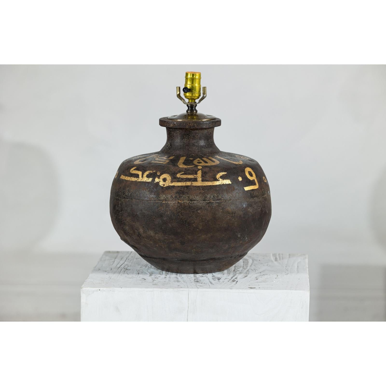 Close-up of vintage dark patina metal jug lamp with yellow script and brass socket, suitable for boho style decor.