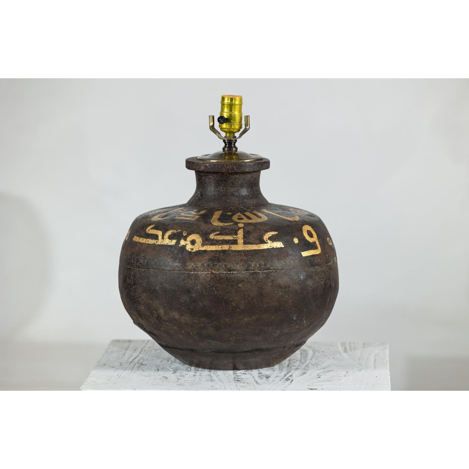 Close-up of a vintage metal jug lamp with painted script, rustic finish, and brass light socket.