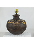Close-up of a vintage metal jug lamp with painted script, rustic finish, and brass light socket.