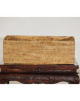 Brown handwoven rattan rectangular basket with side handles on dark carved wooden table, close-up view.
