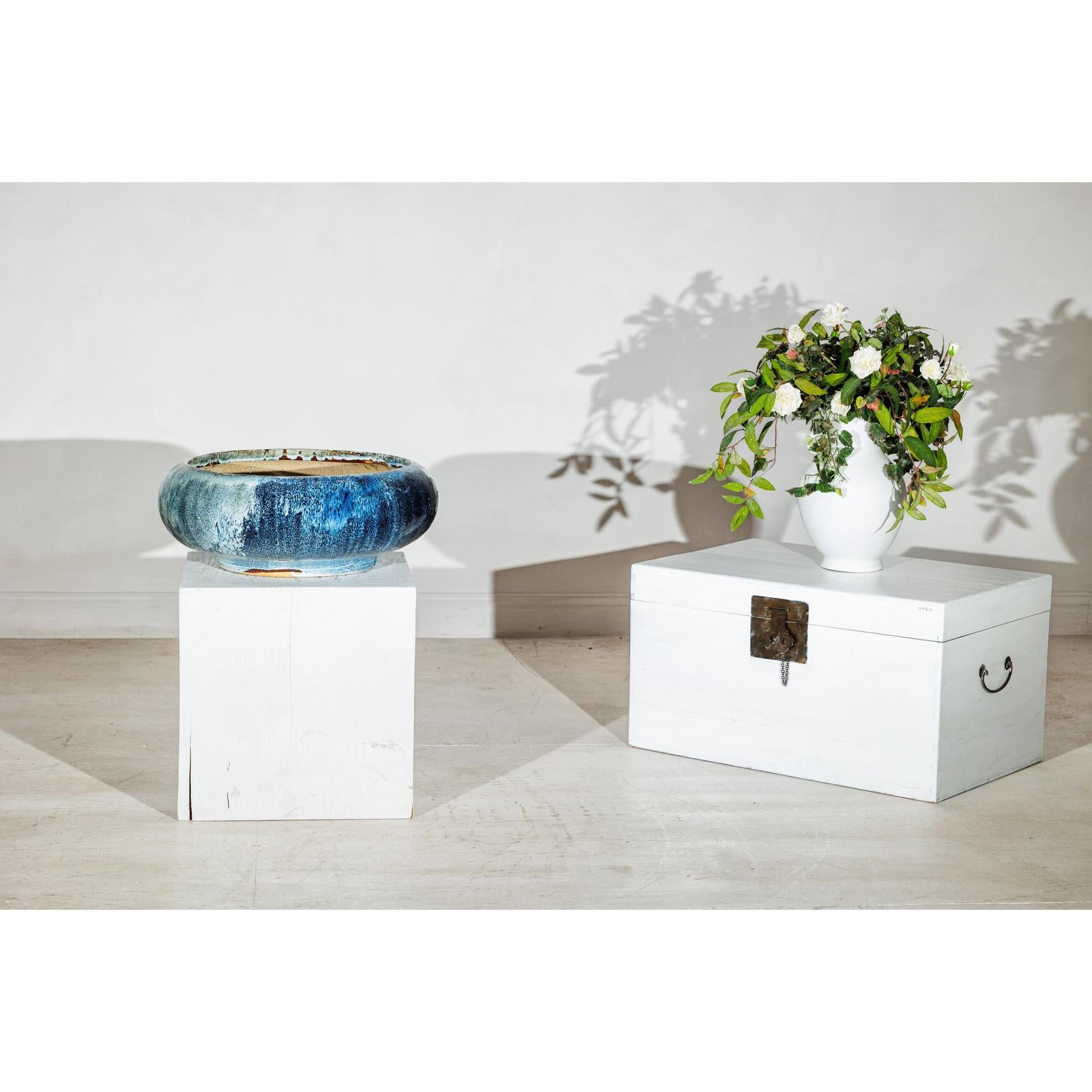 Close-up of a vintage Shigaraki style low blue ceramic planter with wide opening on white wooden boxes against plain background.