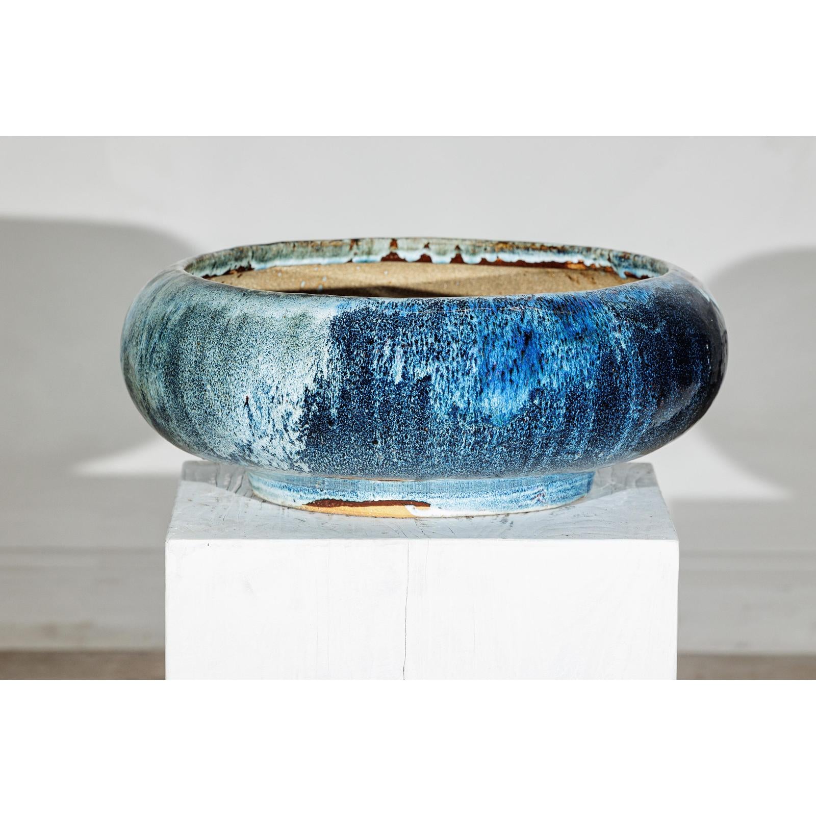 Close-up of a vintage blue Shigaraki style ceramic planter with wide opening on a white pedestal against plain background.