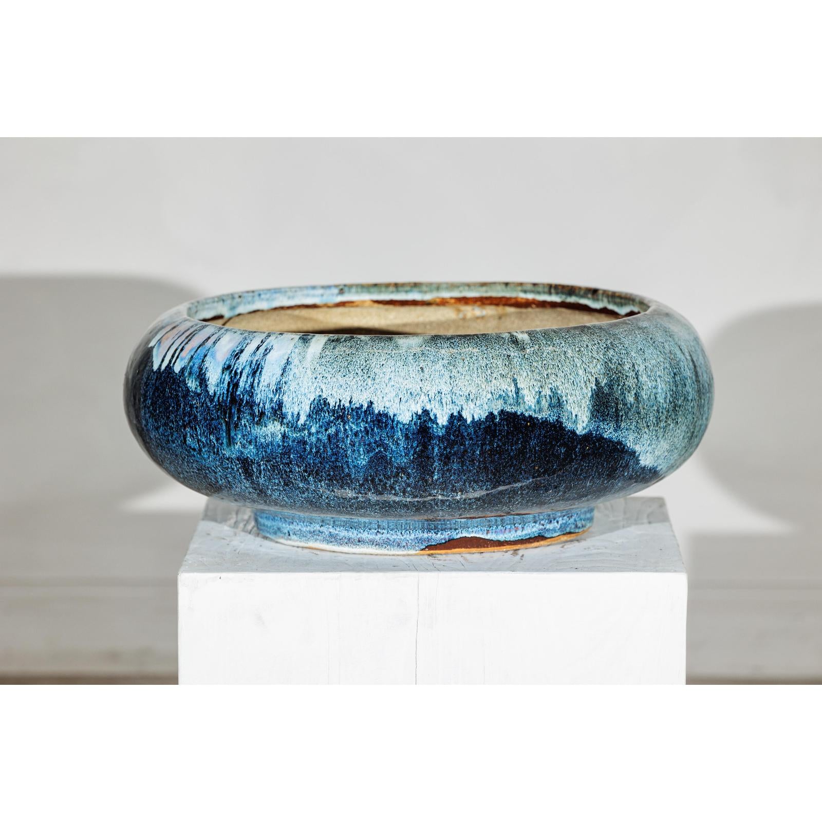 Blue ceramic Shigaraki-style low planter with wide opening on a white pedestal, plain background.