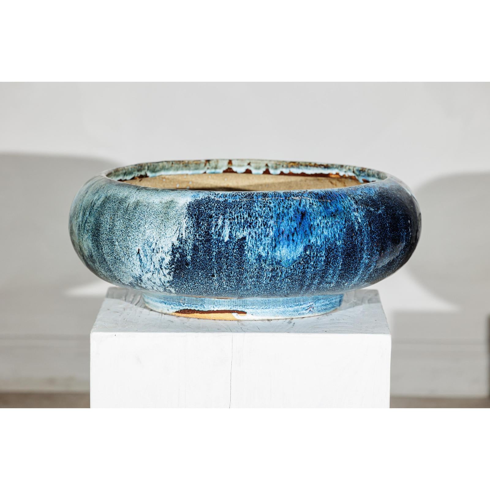 Blue ceramic Shigaraki-style low planter with wide opening on white pedestal, plain background.