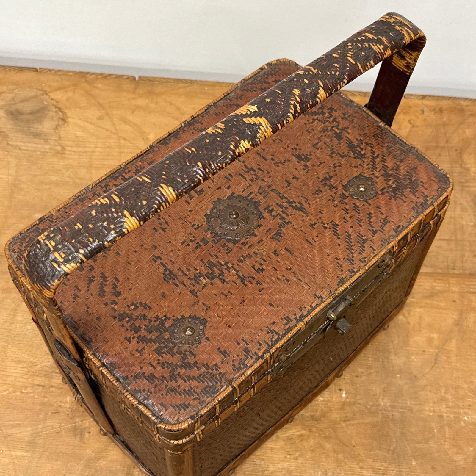The Woven Rectangular Picnic Basket with Handle &amp; Hinged Lid features metal accents and a rustic brown-and-yellow pattern, highlighting Southeast Asian craftsmanship as it sits on a wooden surface.