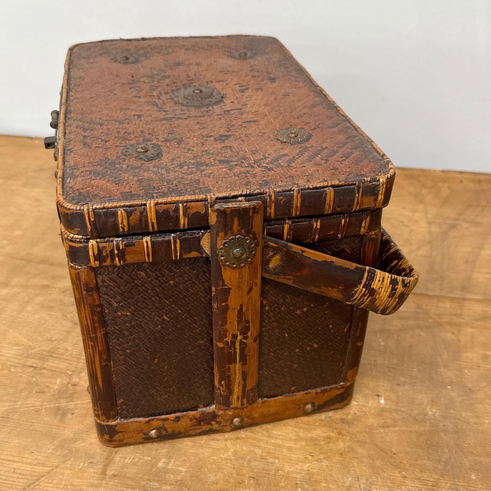 A Woven Rectangular Picnic Basket with Handle &amp; Hinged Lid, featuring decorative metal accents and a rustic finish that showcases classic Southeast Asian craftsmanship, sits gracefully on a wooden surface.