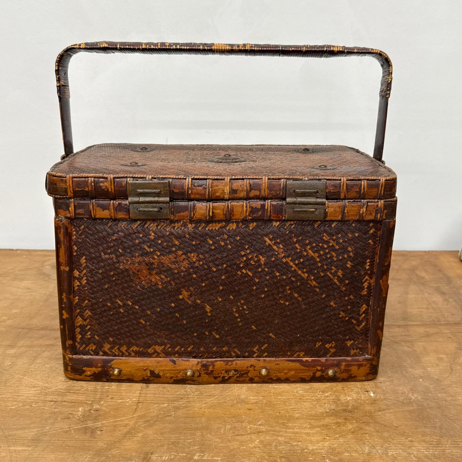 The Woven Rectangular Picnic Basket with Handle &amp; Hinged Lid, crafted from brown rattan with two metal clasps, highlights Southeast Asian artistry as it rests on a wooden surface against a plain light background.