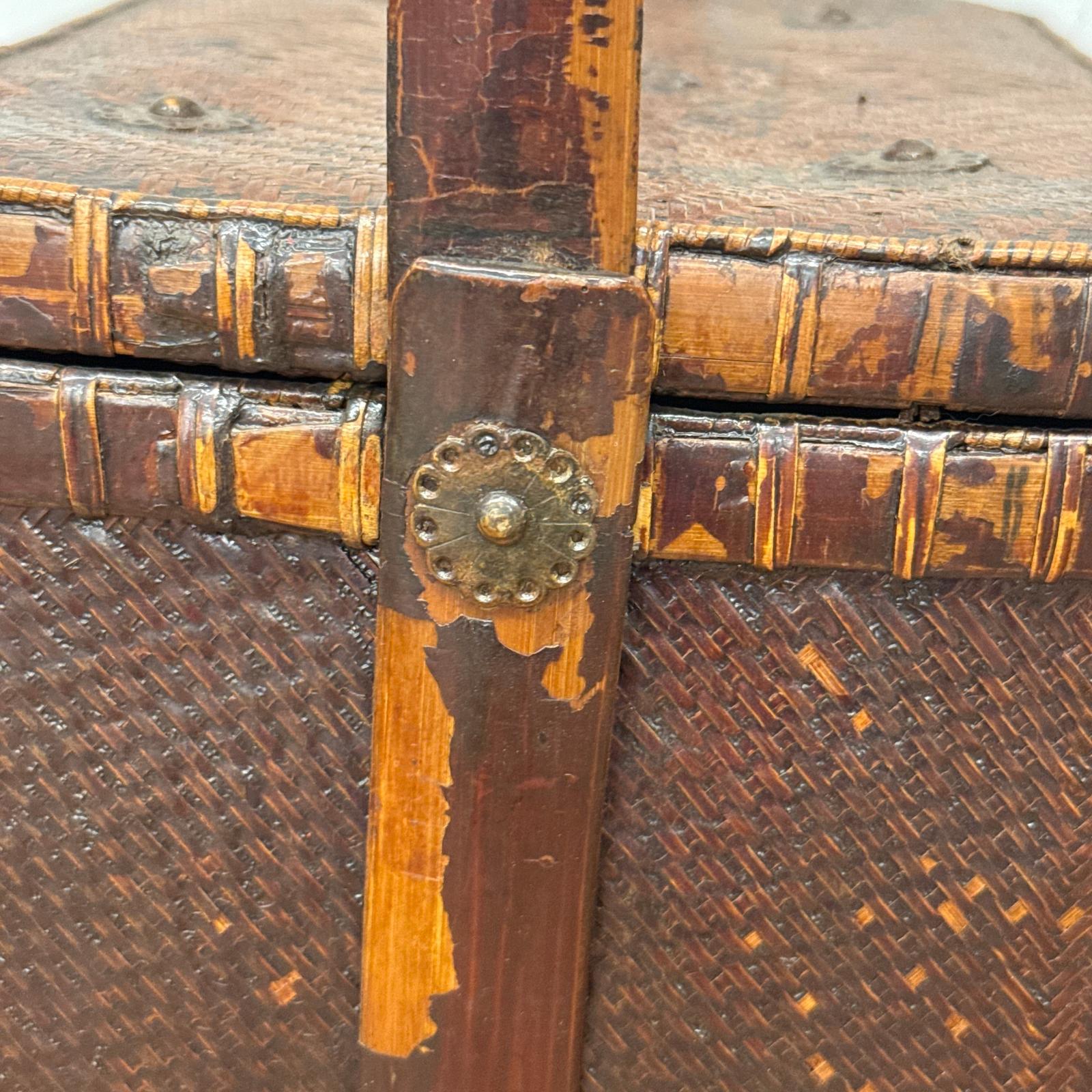 Close-up of the Woven Rectangular Picnic Basket with Handle &amp; Hinged Lid, featuring wood trim and an ornate metal fastener. The chipped finish reveals lighter wood underneath, highlighting its Southeast Asian craftsmanship and unique history.