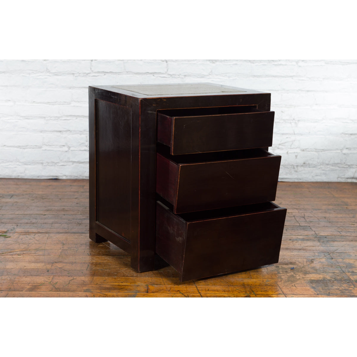 Antique Chinese black lacquer bedside cabinets with Ming Dynasty tops on a wooden floor beside a white brick wall.