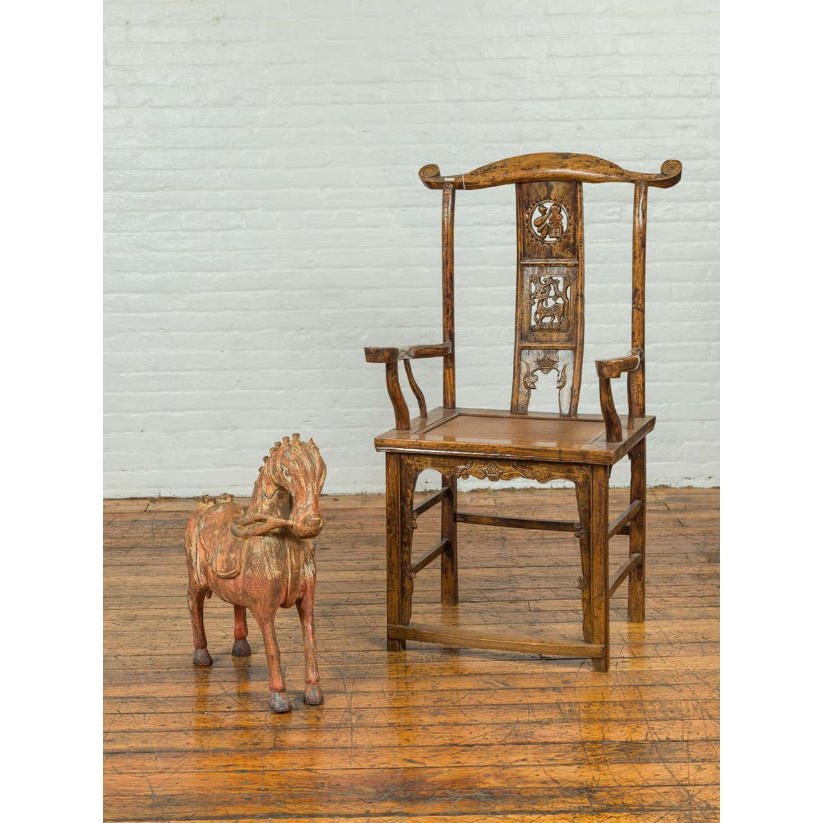 Brown antique wooden armchair next to a small vintage Indian rust-carved horse from Madras on polished wood floor.