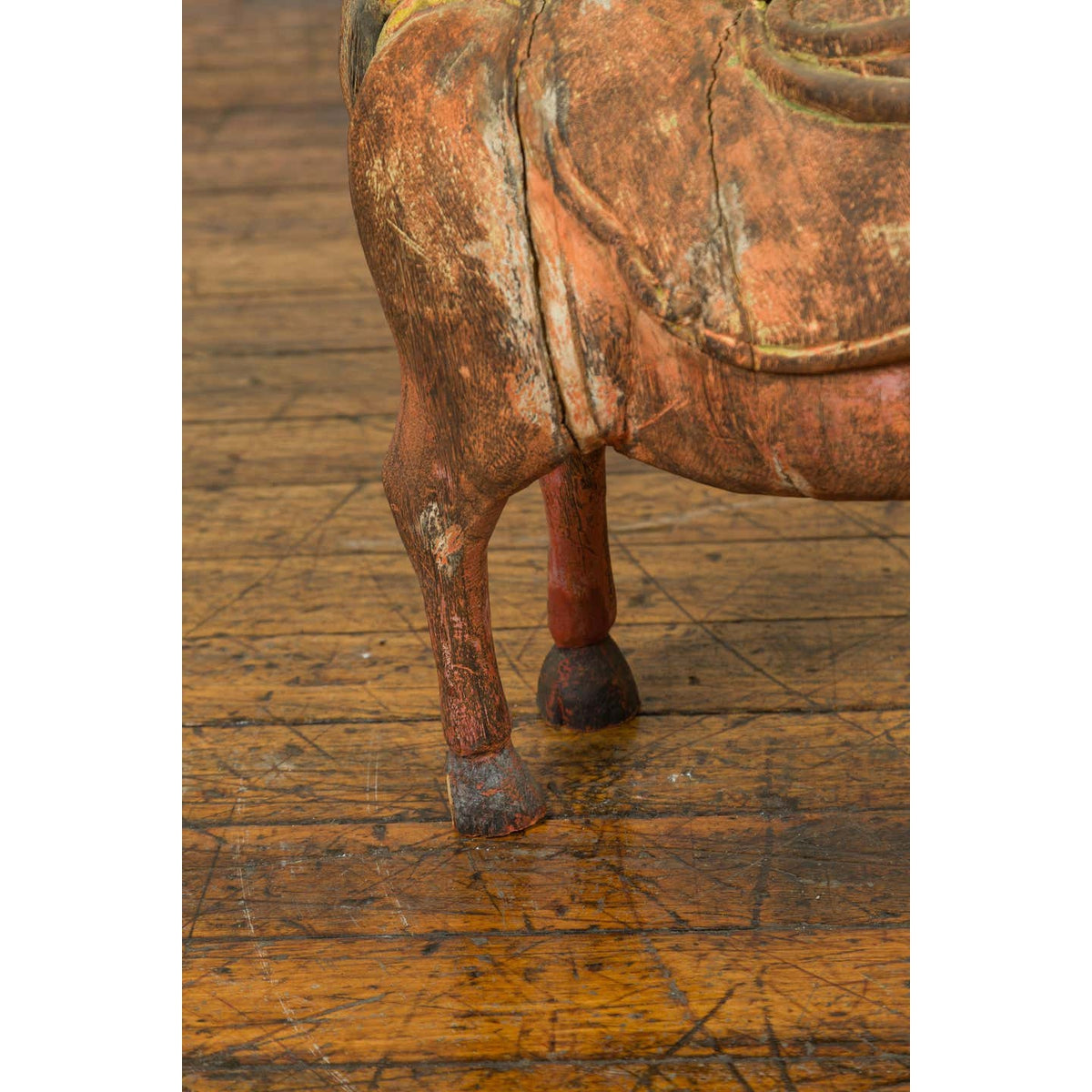 Close-up of a rust-colored carved wooden horse figurine from Madras on a scratched floor.