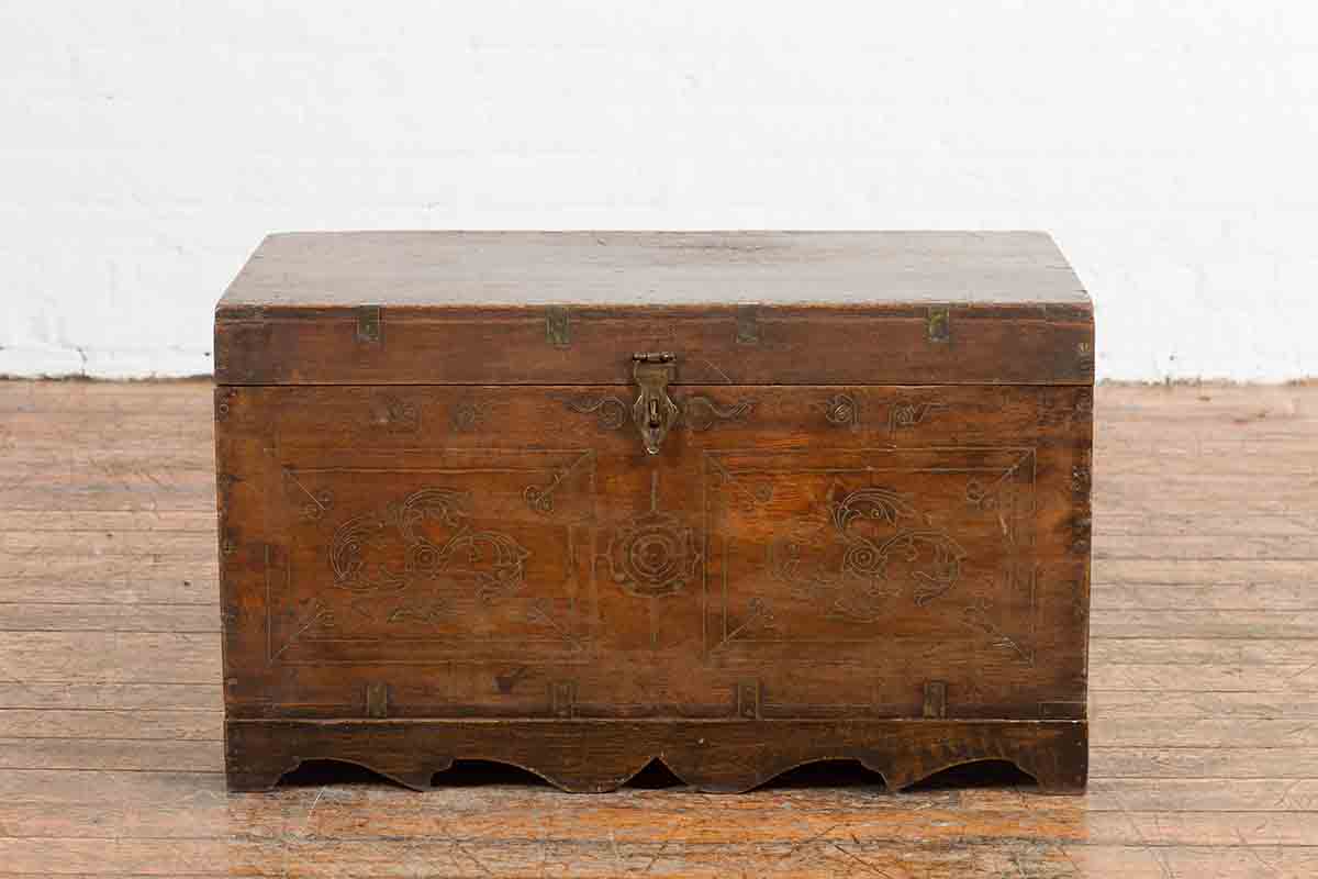 Brown wooden Indian vintage wedding chest with brass foliage décor and multiple compartments on wooden floor by white wall.