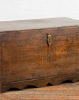 Brown wooden Indian vintage wedding chest with brass foliage décor and compartments on wooden floor against white wall.