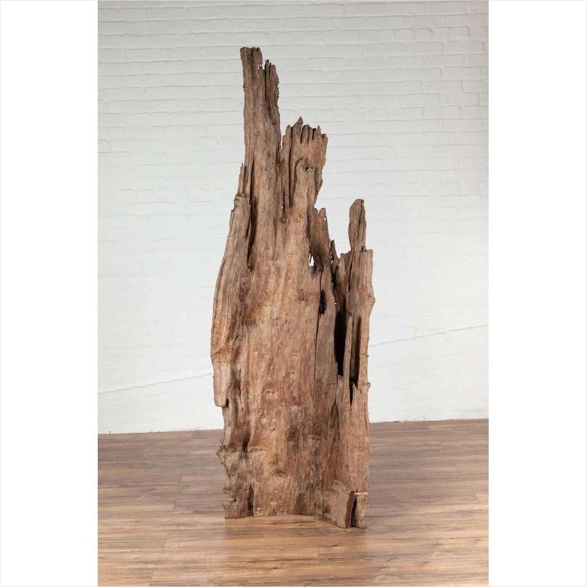 Brown driftwood carving from Northern Thailand on wooden floor against a white brick wall, Chiang Mai style decor.