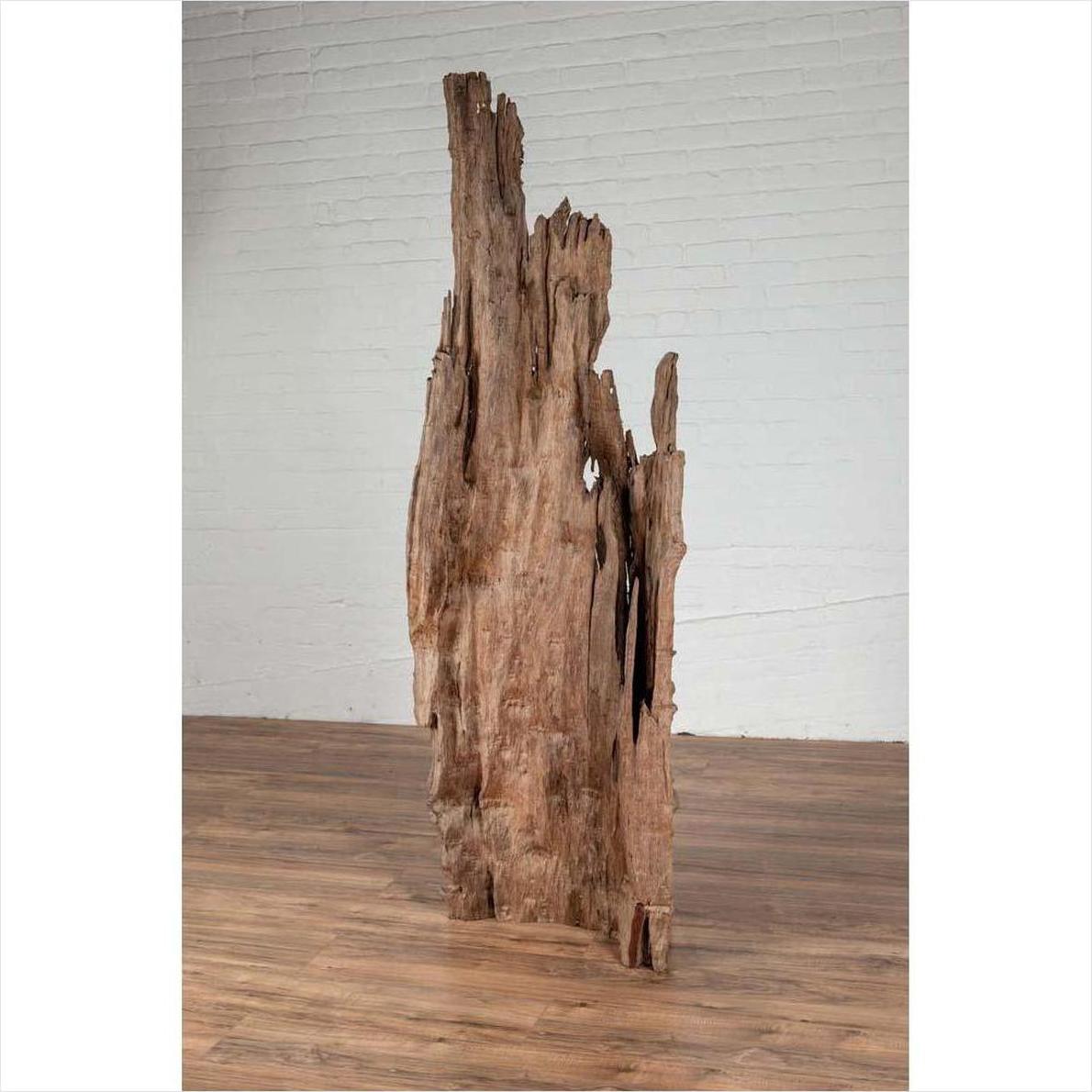 Brown driftwood carving from Northern Thailand on wooden base, placed in front of a white brick wall.