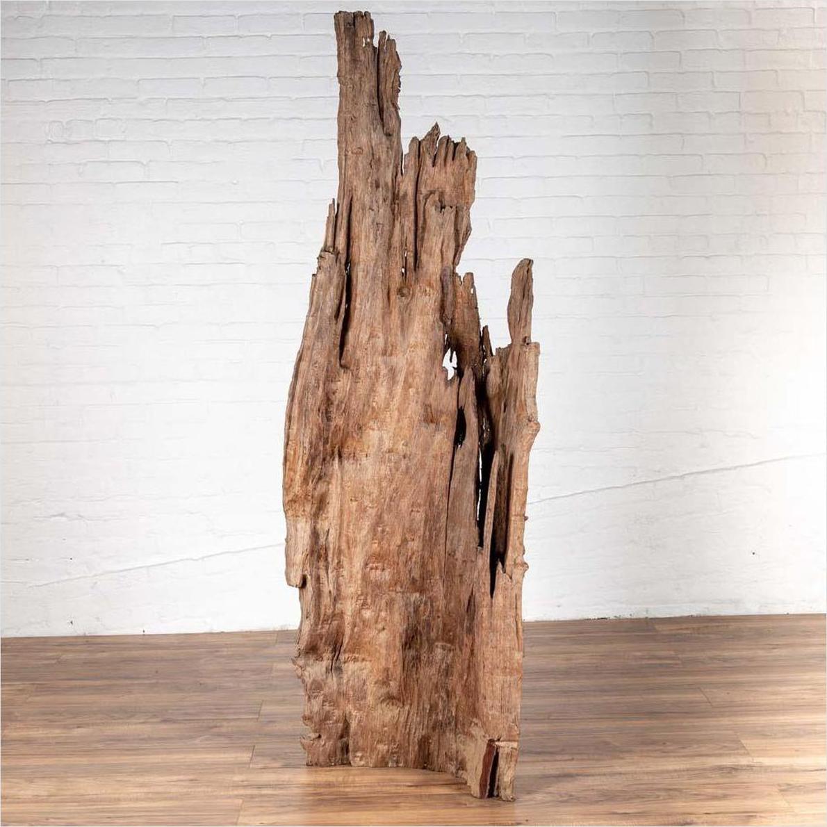 Brown driftwood carving from Northern Thailand on a wooden floor with a white brick wall background.