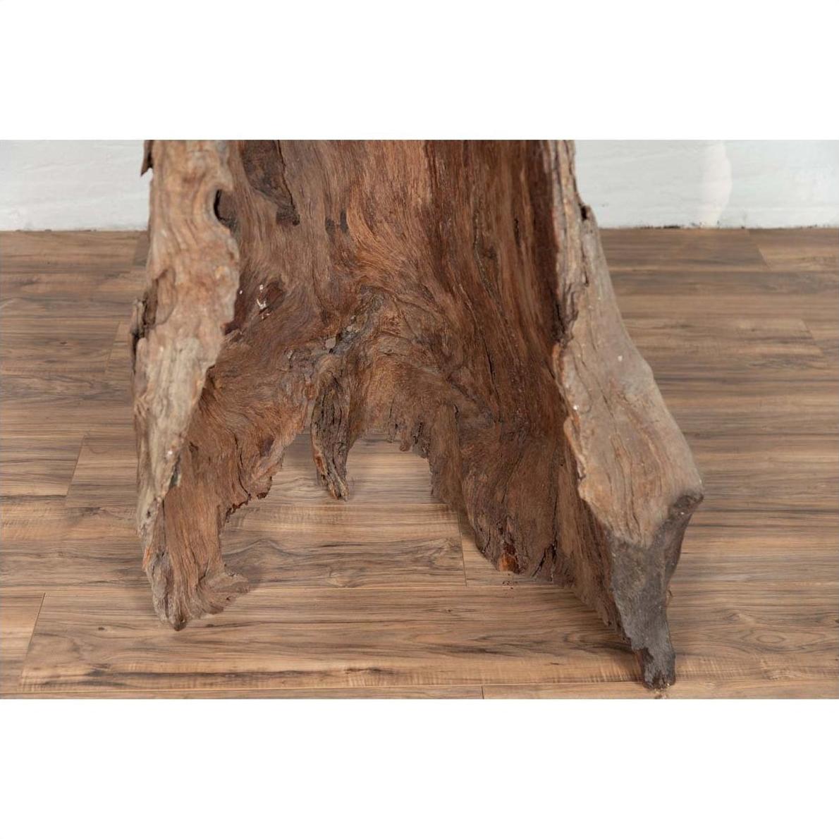 Brown driftwood carving, wood sculpture from Northern Thailand, displayed against a white brick wall indoors.