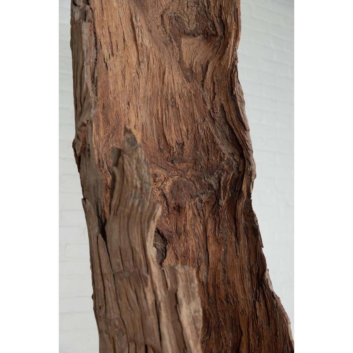 Brown driftwood close-up carving, ancient wood material, displayed against a brick wall background indoors.