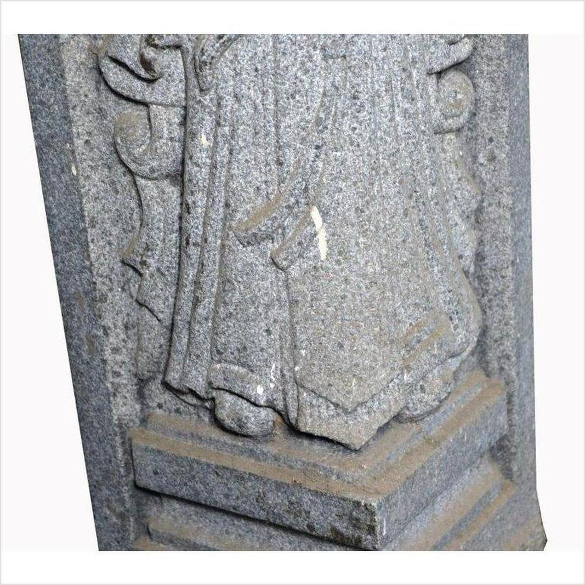Close-up of gray stone Chinese guardian sculpture, hand-carved, showing robed legs and base.