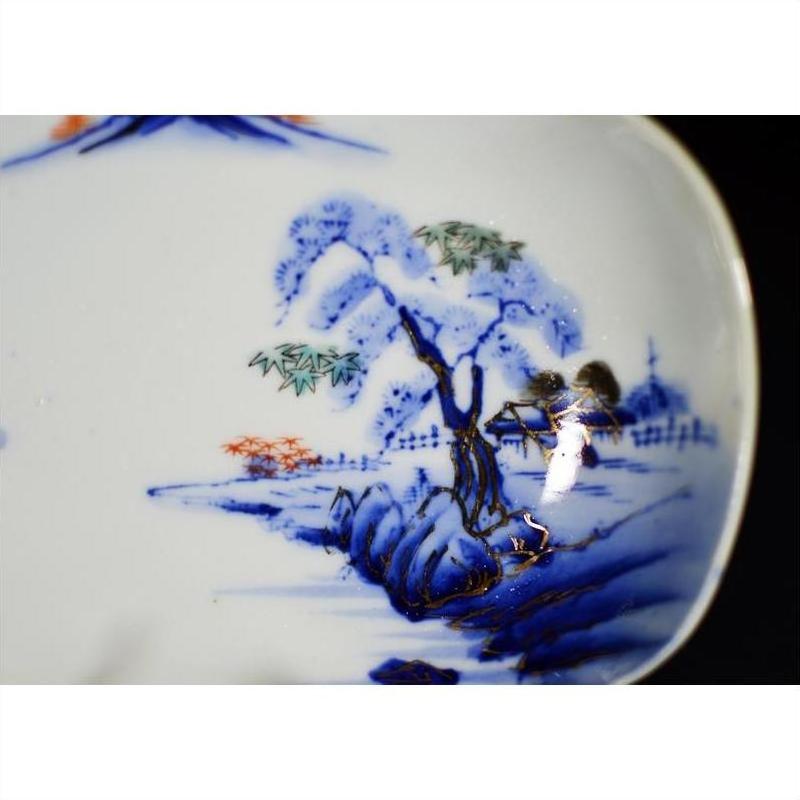 Close-up of blue and orange hand painted porcelain bowl with landscape, tree, and distant buildings design, antique Asian style.