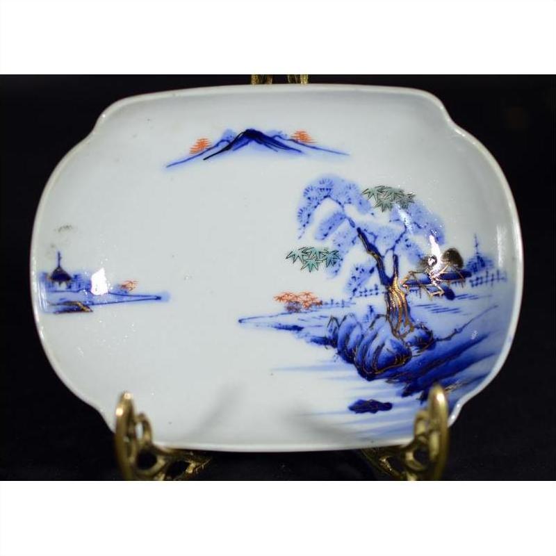 Blue and orange hand painted porcelain bowl with mountain, tree, and water landscape on display stand.