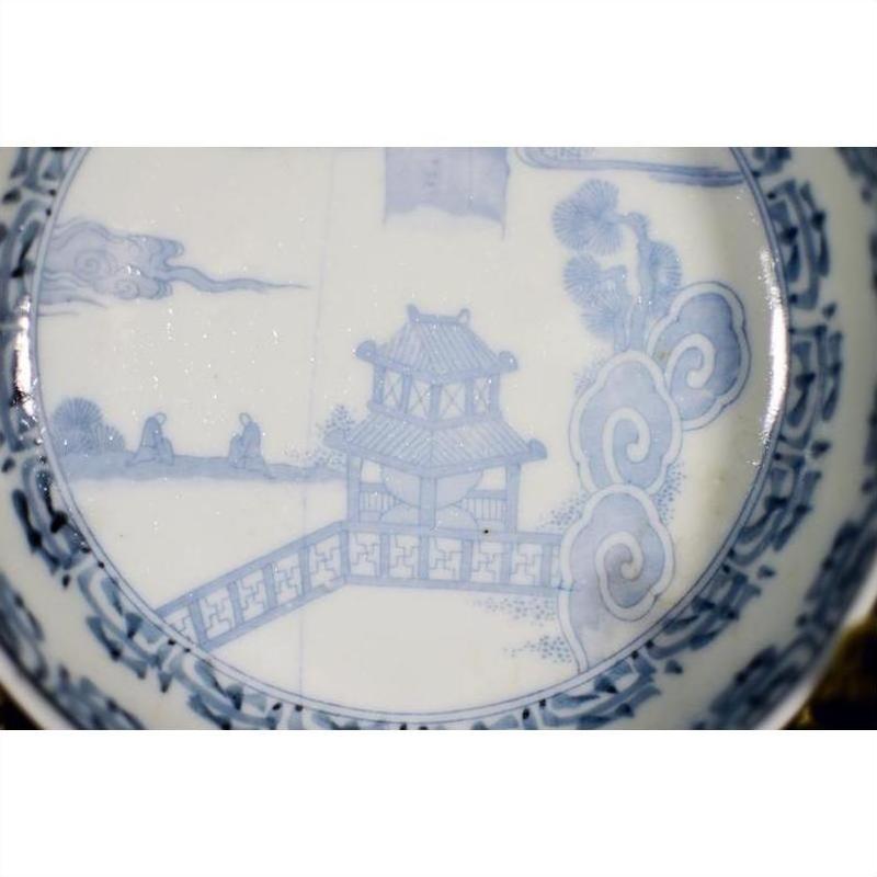 Blue and white porcelain bowl with hand painted pagoda, trees, and figures in traditional Asian landscape style.