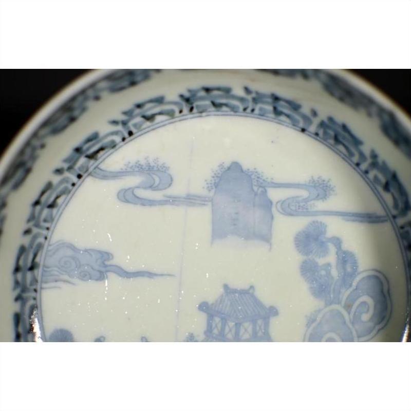 White porcelain bowl with intricate hand painted Asian landscape and architectural designs near the rim, close-up.
