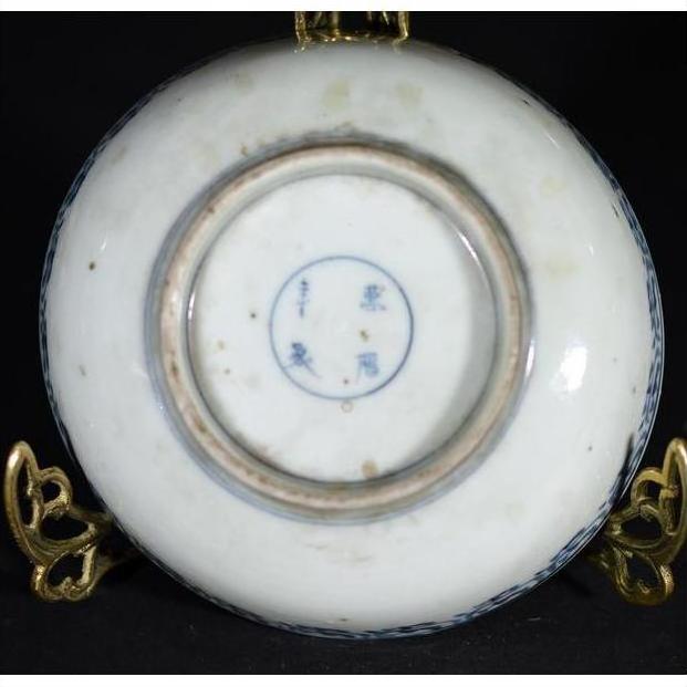 Close-up of the underside of a white porcelain bowl with blue markings, resting on a gold stand.