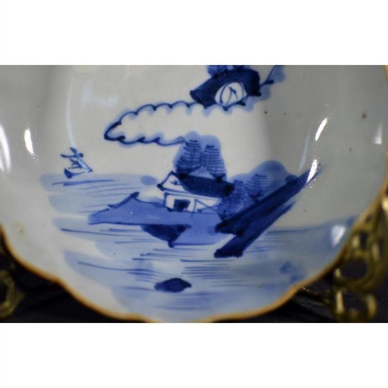 White porcelain bowl with hand painted house, trees, sailboat by water, and gold rim accents, close-up.