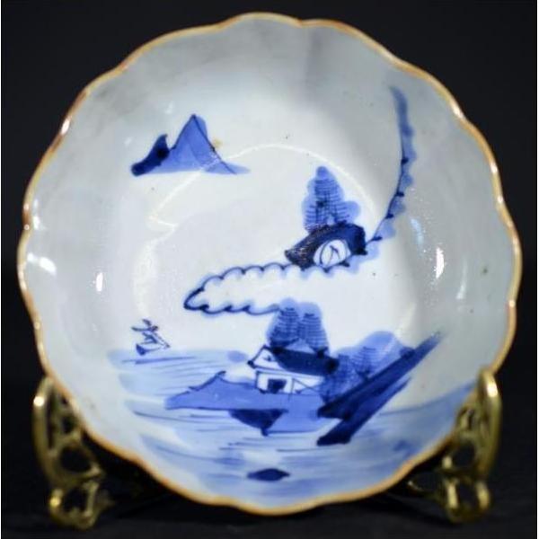 Close-up of blue and white hand painted porcelain bowl with mountain landscape motifs on ornate gold stand.