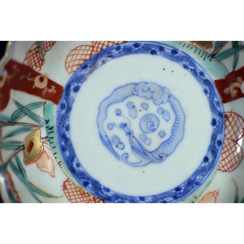Close-up of antique Asian porcelain bowl base with blue circle and red, green, gold hand-painted floral accents.