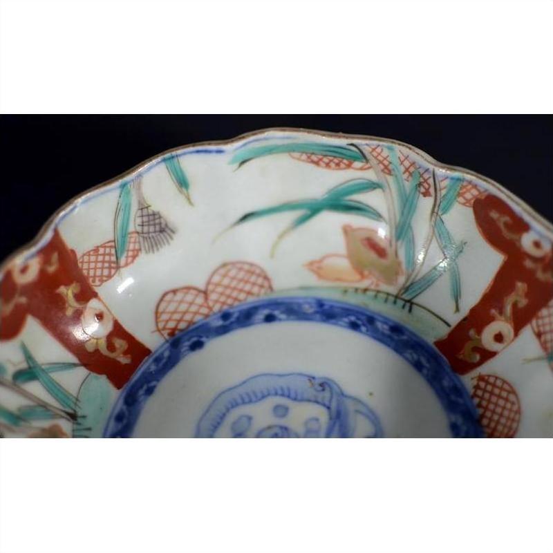 Close-up of an antique Asian porcelain bowl with hand painted red, green, blue, and gold designs.