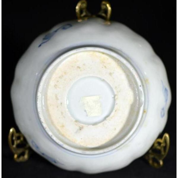 Close-up of the underside of an antique hand painted Asian porcelain bowl with a small square sticker on metal stand.
