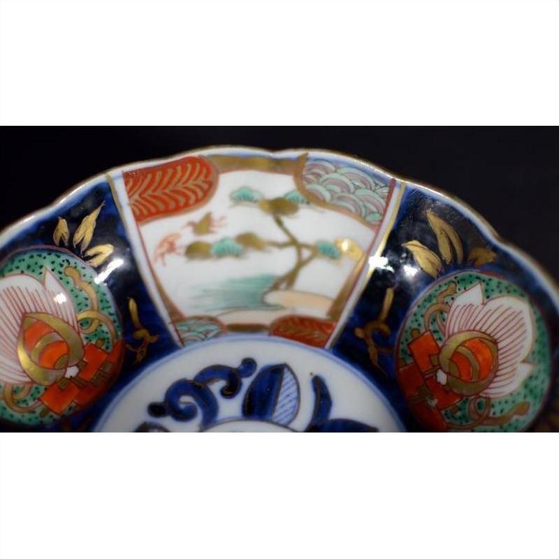 Close-up of a red, green, gold, and blue hand painted porcelain bowl with floral and landscape designs.