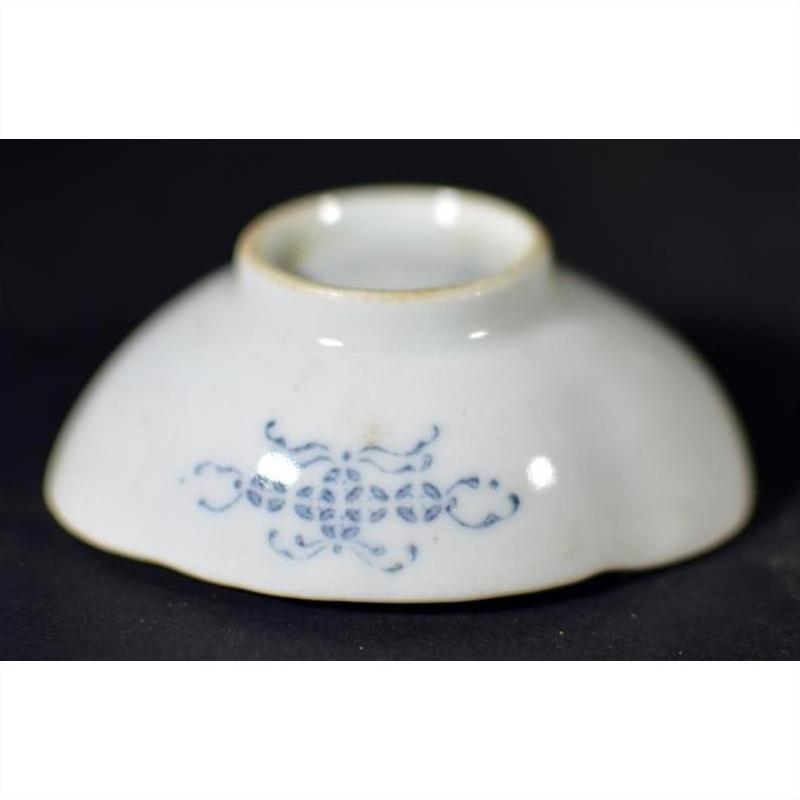 Close-up of blue and white hand painted porcelain dish, upside down, with intricate side pattern on dark background.