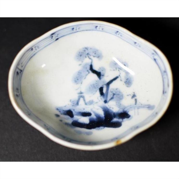 Blue and white porcelain dish with hand painted landscape, wavy rim, close-up against a moody background.