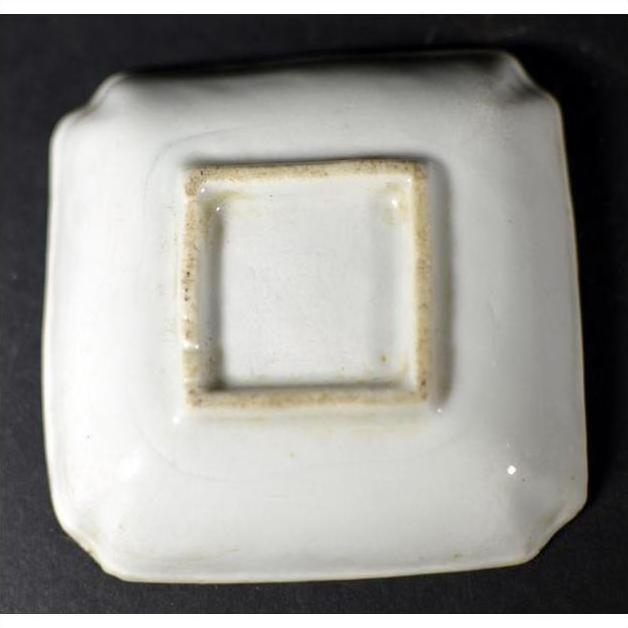 White porcelain dish, hand-painted, shown upside down with unglazed recessed base on dark background, close-up.