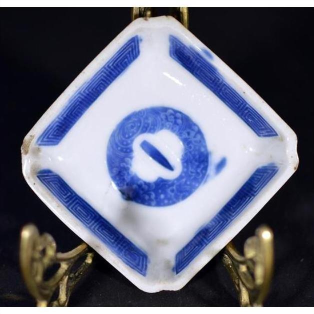Blue and white hand painted porcelain dish with central symbol, displayed on a brass stand.