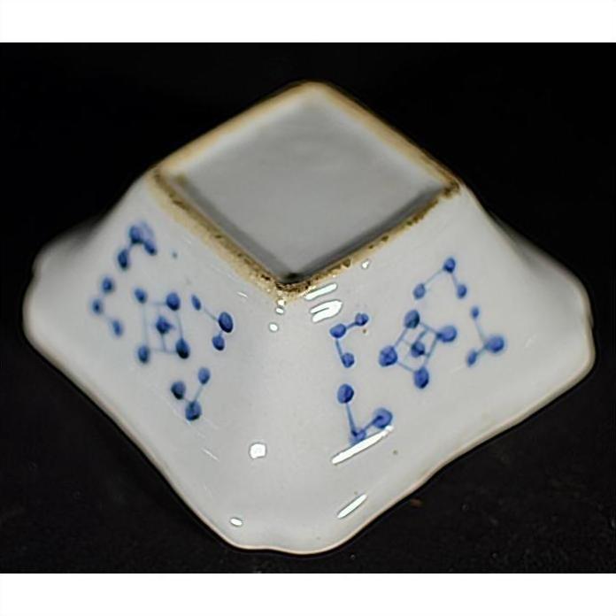 Close-up of an antique Asian porcelain dish with blue dotted sides on a black background.