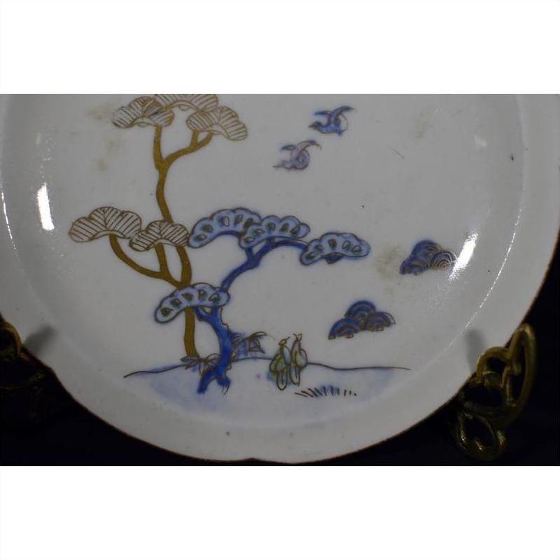 White porcelain plate with hand-painted birds, twin pine trees, and abstract cloud patterns, close-up view.