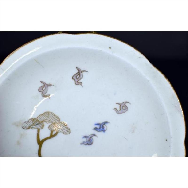 White porcelain plate with gold rim, hand painted soaring birds and twin pine trees, antique Asian design, close-up.