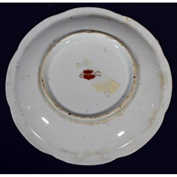Close-up of the bottom of an antique Asian porcelain plate with a small red mark and light center discoloration.