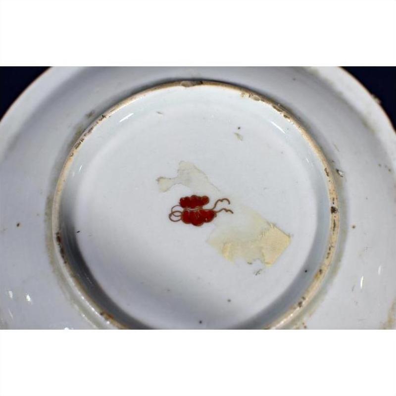 Close-up of base of antique Asian porcelain plate with red floral mark and chipped glaze.