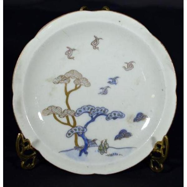 White porcelain plate with hand painted soaring birds and pine trees on brass stand, close-up.
