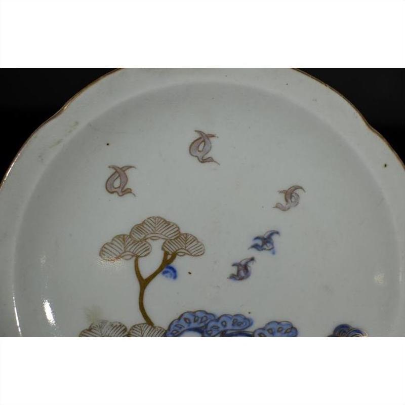 Blue and gold porcelain plate with windswept pines and stylized birds on white background, close-up.
