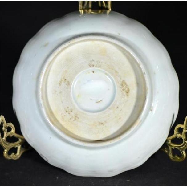 Close-up of the bottom of an antique porcelain plate with Asian hand-painted design, displayed on a metal stand.