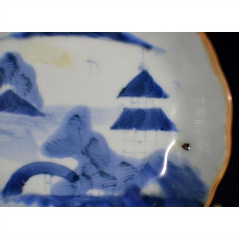 Blue and white porcelain plate with misty peaks, arched bridge, mountains, trees, and dark spot on right side.